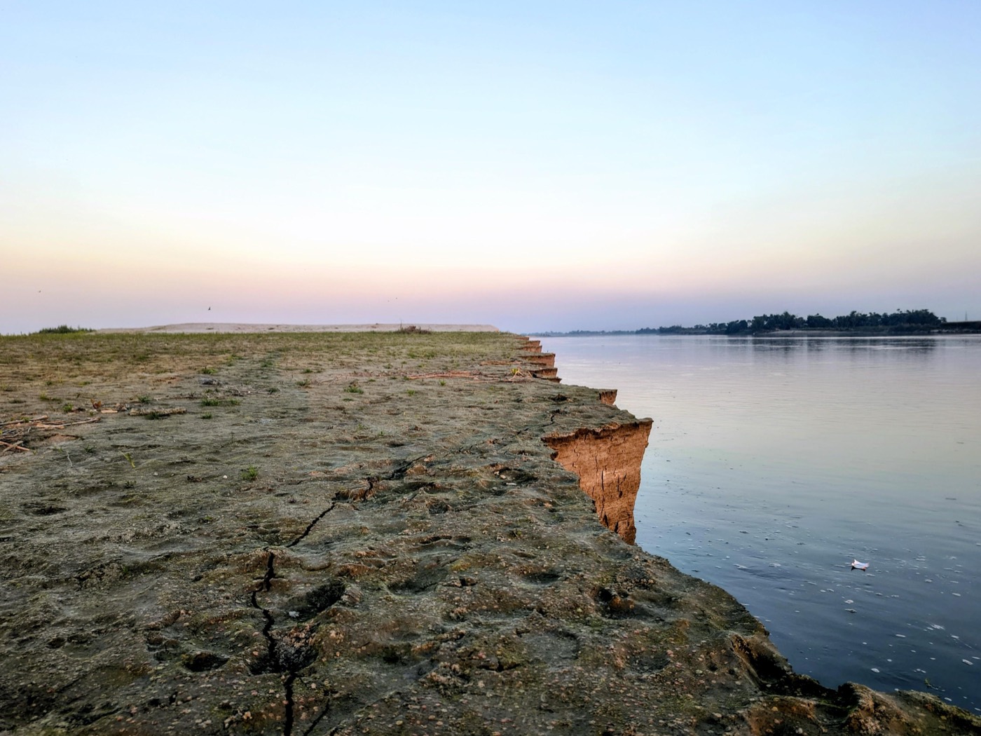 Eroding land crumbling at the edge of the water at dusk